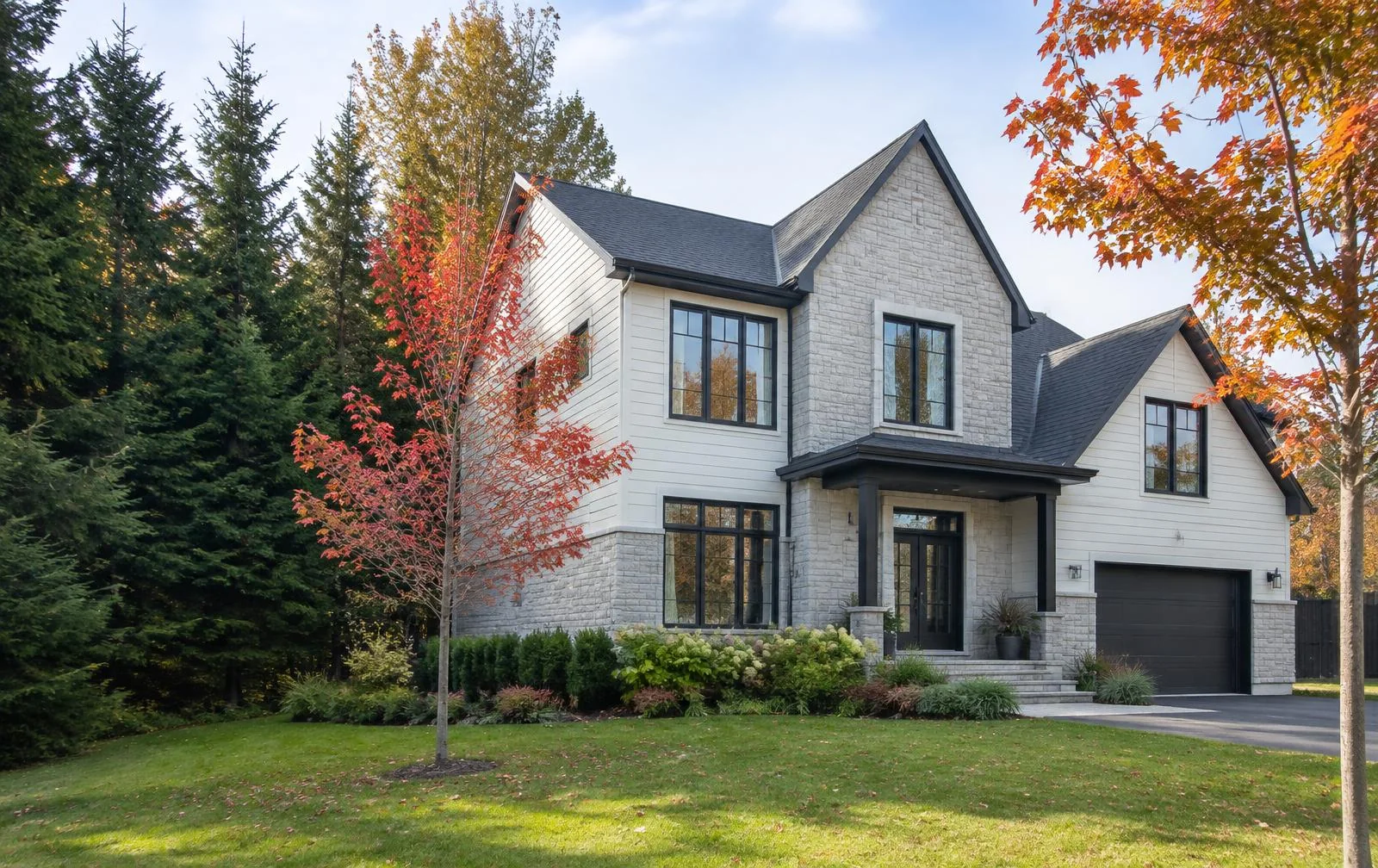 Maison québécoise en pierre et parement clair avec de grandes fenêtres propres, entourée d’érables en automne